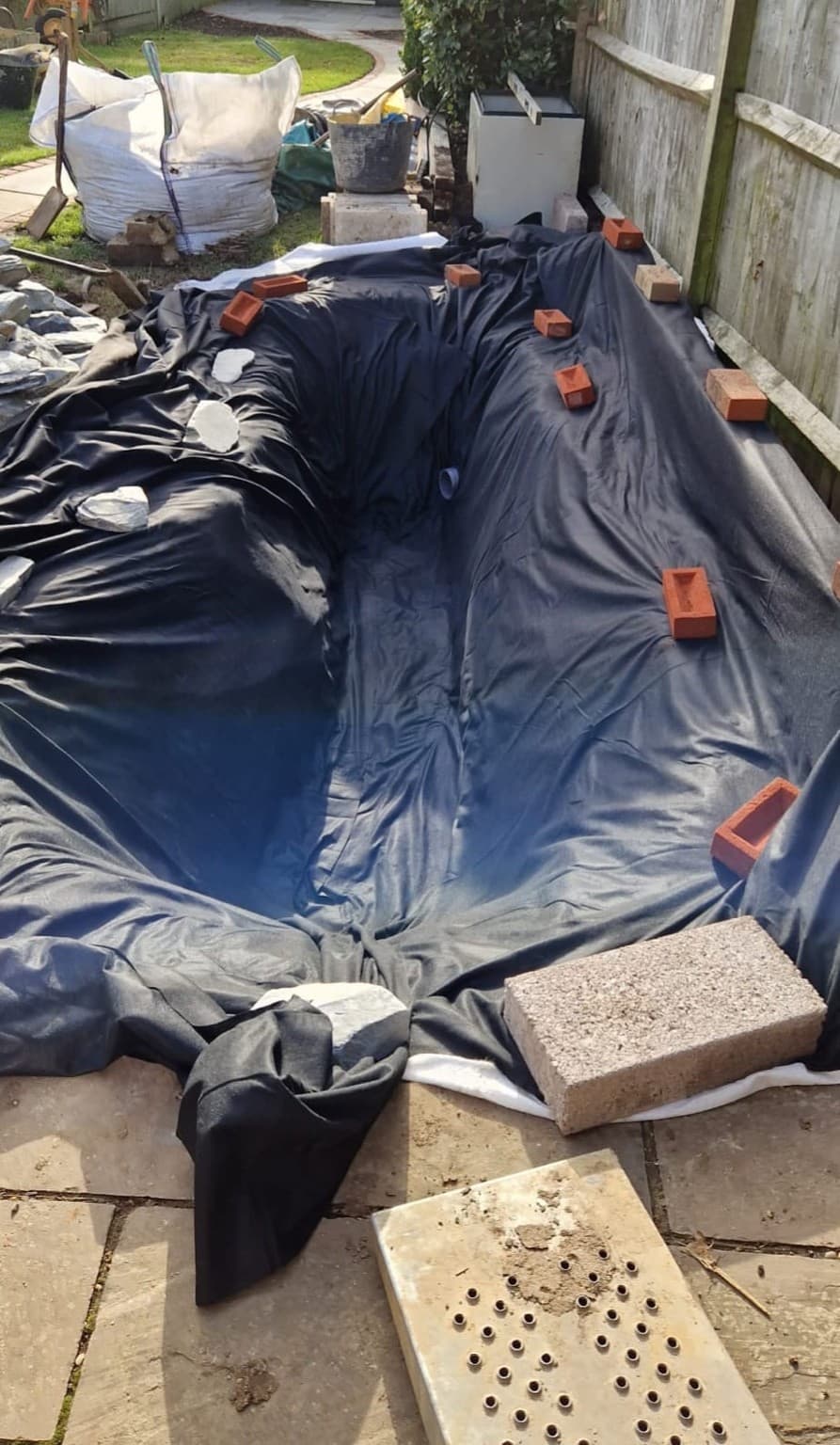 Before – pond excavation lined with protective underlay and pond liner held in place with bricks in a Brighton garden.